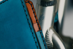 detail shot of stitching blue exterior and brown interior leather wallet with four card pockets next to bicycle