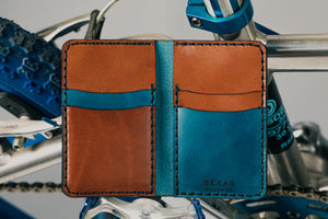 blue exterior and brown interior leather wallet with four card pockets next to bicycle tire