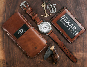  brown leather phone sleeve with card sleeve next to leather watch band and matching slim wallet