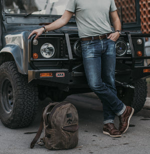 Adult male leaning on classic 4x4 showcasing dark brown leather belt. Backpack can be seen in the foreground