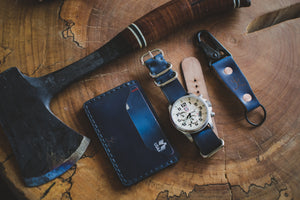 blue cordovan and brown leather two pocket slim wallet next to matching watch, keychain, and axe