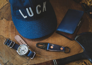 blue cordovan and brown leather four pocket vertical wallet next to blue cap and matching watch strap and keychain