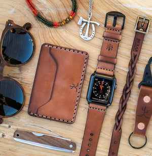 Whiskey cordovan and brown leather two pocket slim wallet next to watch, keychain, knife, necklace, sunglasses