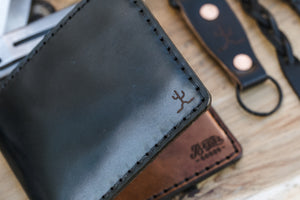 detail of laser engraved cactus on black cordovan leather exterior with black cow leather interior two card pocket slim wallet next to keychain and watch strap