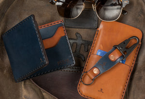 folded blue and brown leather four card pocket bifold wallet next to phone wallet, keychain, and sunglasses