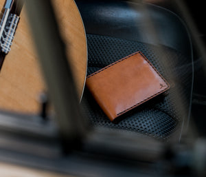 brown leather six card wallet sitting on sports car seat next to guitar