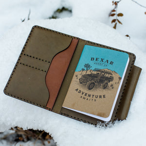 green and brown leather notebook wallet with two card pockets placed in snow 