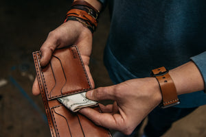 interior of brown four card pocket and two stash pockets with cash displayed and held with someone wearing leather bracelets and watch