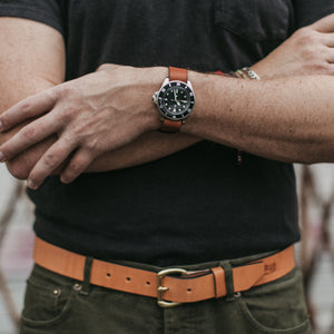 Closeup of adult male crossed arms with a tan leather watch strap and tan leather belt