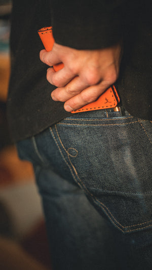 four pocket vertical orange leather wallet  going into mans pocket