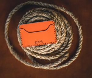 two pocket slim orange leather wallet next to twine rope