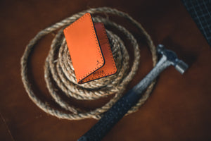 four pocket vertical orange leather wallet  next to hammer and twine rope