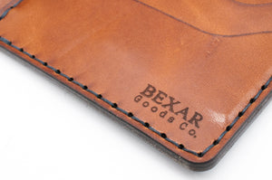 detail of laser engraved bexar logo on blue cordovan and brown leather four pocket bifold wallet