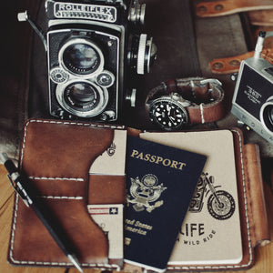 leather notebook wallet with two card pockets and pen sleeve next to cameras and leather watch strap