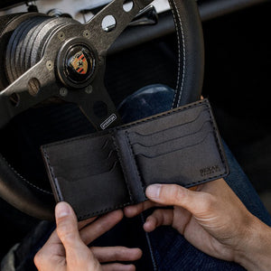 man holding black leather six card pocket bifold wallet in sports car
