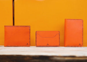 Orange four pocket bifold wallet next to two pocket slim wallet and four pocket vertical wallet
