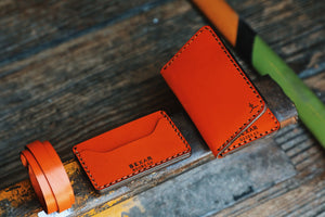 array of orange leather gear next to four pocket vertical orange leather wallet 