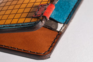 detail of laser engraved piece on multicolor four pocket vertical wallet with red, blue, yellow, and cowprint leather