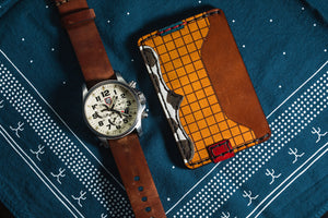 multicolor leather two pocket card wallet with cowprint next to analog watch with leather band