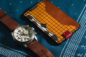 multicolor leather two pocket card wallet with cowprint next to analog watch with leather band