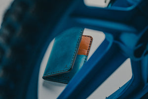 blue exterior and brown interior leather wallet with four card pockets next to bicycle tire