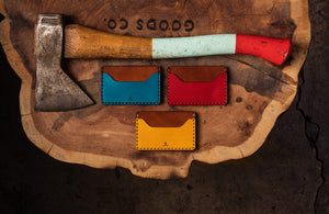 leather wallet with two pocket with one center divider- shown in yellow, blue, red, next to axe