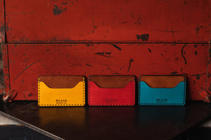 three wallets with two pocket with one center divider shown in yellow, red, blue leather with brown interior