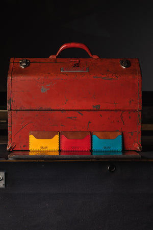 three wallets with two pocket with one center divider shown in yellow, red, blue leather with brown interior