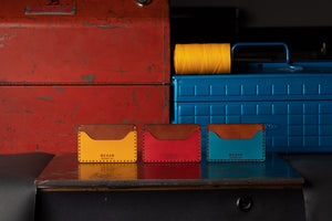three leather wallets in yellow, blue, red colors with brown interior all with two pockets and one divider next to toolbox