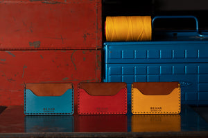 leather wallet with two pocket with one center divider- shown in yellow, blue, red, next to toolbox