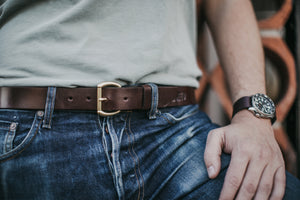 Closeup of adult male standing with hand on thigh showcasing brown leather belt with brass hardware