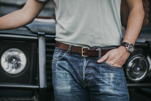 Adult male leaning on classic 4x4 with hand in blue jean pocket showcasing brown leather belt with brass buckle