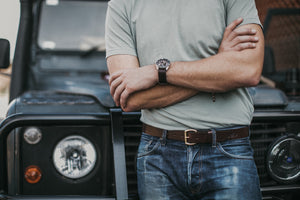 Adult male leaning on classic 4x4 emphasizing dark brown leather belt on blue jeans