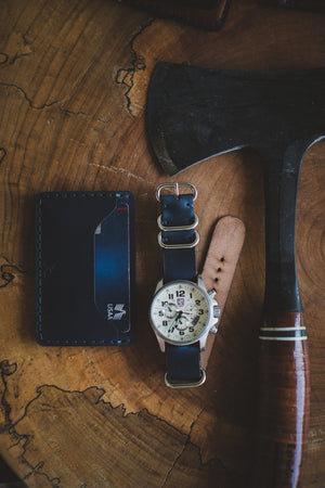 blue cordovan and brown leather two pocket slim wallet next to watch and axe