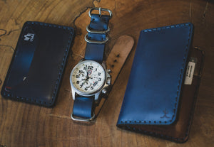 blue cordovan and brown leather two pocket slim wallet next to matching wallet and watch stra[
