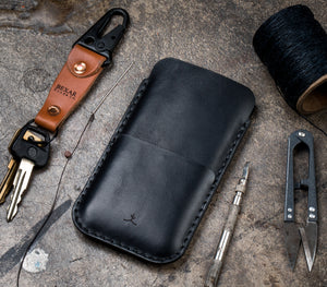 black leather phone sleeve with card pocket next to keychain and leather tools