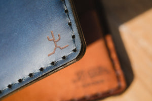 detail of cactus engraving on blue cordovan and brown leather four pocket vertical wallet