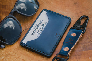 blue cordovan and brown leather two pocket slim wallet next to keychain and sunglasses