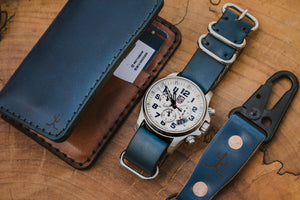 blue cordovan and brown leather four pocket vertical wallet next to matching watch strap and keychain