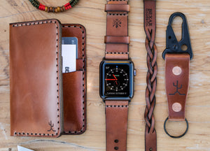 overlay of whiskey cordovan leather with brown interior four pocket vertical wallet next to watch, leather bracelet, and keychain