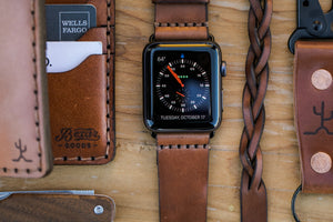 Whiskey cordovan and brown leather six pocket bifold wallet next to watch, bracelet, keychain