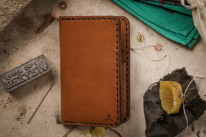 exterior view of brown leather vertical wallet surrounded by leather making tools