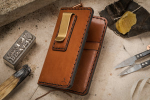 brown leather four pocket vertical wallet with brass money clip on exterior surrounded by leather making tools