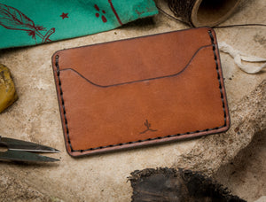 overview of brown leather two pocket wallet surrounded by some of the tools used to make wallet