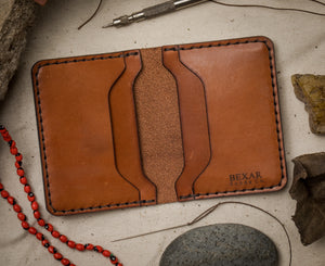 open interior view of brown leather four pocket folding wallet with brass money clip next to leather making tools
