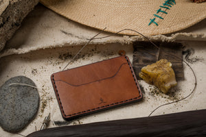 overview of brown leather two pocket wallet surrounded by some of the tools used to make wallet