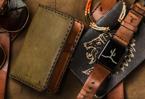 green and brown leather four card vertical wallet next to watch and sunglasses