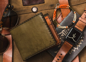green exterior and brown interior leather four pocket bifold wallet next to watch and sunglasses