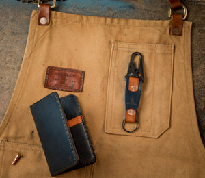 folded view of blue and brown leather  four pocket vertical wallet next to keychain on top of canvas apron