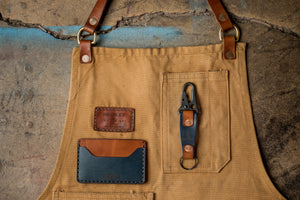blue and brown leather two pocket slim wallet next to keychain on top of canvas apron
